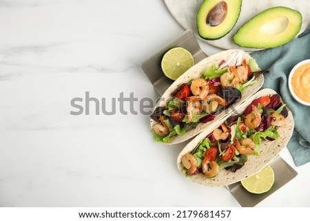 Delicious tacos with shrimps, lime and avocado on white table, flat lay. Space for text