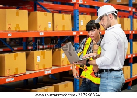 A man and women in charge of a large warehouse is checking the number of items in the warehouse that he is responsible for