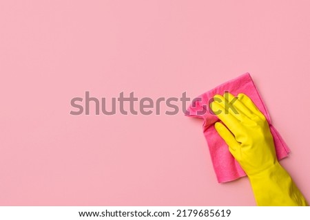 Employee hand in yellow rubber protective glove hold red or pink rag wiping pink wall background. House cleaning service, general or regular cleanup concept. Empty place for text or design Royalty-Free Stock Photo #2179685619