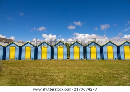 Shades of blue. A day in the british south coast, in Felpham, near brighton. Beautiful brighty colored blue and yellow beach huts in the lawn bhind the beach. British summer atmosphere.