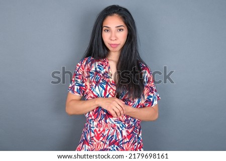 Photo of cheerful confident young beautiful brunette woman wearing colourful dress over white wall arms together