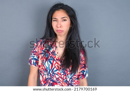 Displeased young beautiful brunette woman wearing colourful dress over white wall frowns face feels unhappy has some problems. Negative emotions and feelings concept