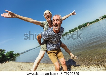 Portrait of happy mature man being embraced by his wife at the beach. 