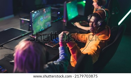African american bearded casually dressed man wearing headset playing a popular online team game, doing a fist bump with another player. High quality photo