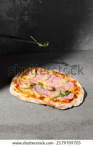 Cooked Italian pizza with ham and artichokes on dark background. Pinsa with ham on gray stone table with hard shadow. Roman pizza with ham and artichokes on concrete background. Pinsa from chef
