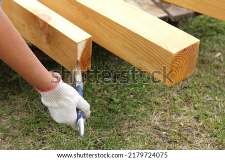 a hand in a protective glove holds a brush against the background of wooden structures. protective impregnation of wood Royalty-Free Stock Photo #2179724075