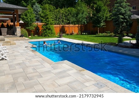 Mother and daughter swimming in new back yard pool with  patio of pavers and green lawn and gardens Royalty-Free Stock Photo #2179732945