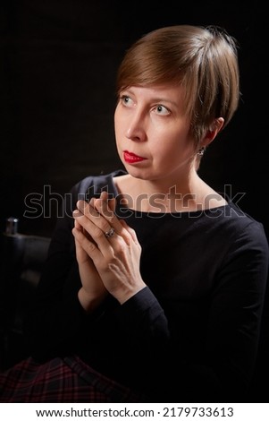 Dark portrait of serious young woman with short blonde hair in studio with black background. Girl model posing during photo shoot