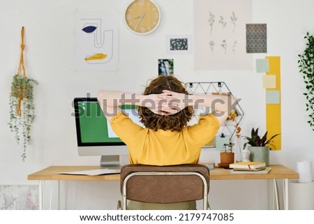 Rear view of young freelance designer having minute of rest while sitting in front of computer monitor and keeping hands behind head Royalty-Free Stock Photo #2179747085