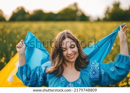 Happy ukrainian woman with national flag on canola blossom meadow background. Portrait of young girl in embroidery vyshyvanka. Ukraine, independence, freedom, patriot symbol, victory in war.