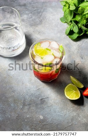 cold detox water with lime, strawberry, mint in the glass with ice cubes on gray background