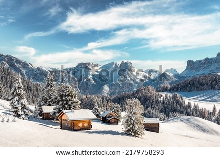 Picturesque landscape with small wooden log cabin on meadow Alpe di Siusi on sunrise time. Seiser Alm, Dolomites, Italy. Snowy hills with orange larch and Sassolungo and Langkofel mountains group Royalty-Free Stock Photo #2179758293