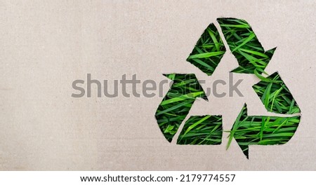 Recycling concept - recycling symbol made in cardboard with plastic, green grass in background