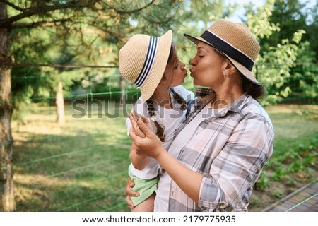 Caucasian little girl kissing her mom while spending time together in family organic vegetable garden on early spring . Horticulture, agricultural hobby, gardening, Earth day, and eco farming concept