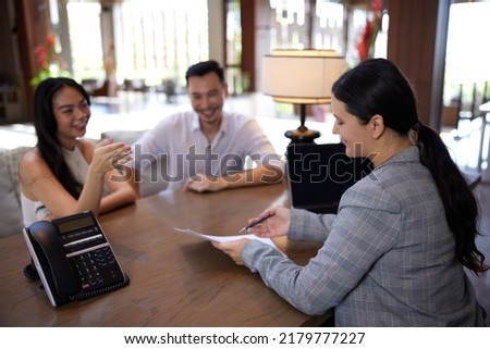 Young happy asian couple talking to banker or consulting agent, making legal deal, taking loan or mortgage, purchasing real estate, new apartment or house