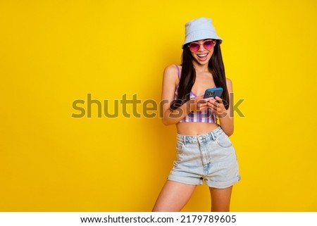 Photo of funny sweet lady wear striped crop top cap dark glasses chatting modern device empty space isolated yellow color background