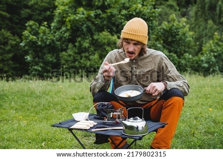 Camping food in nature, cook fried eggs on a gas burner, tourist kitchen at the campsite, guy dining in nature in the forest, kettle metal. High quality photo