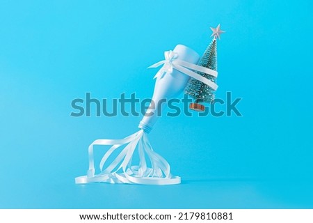 Champagne bottle with green Christmas tree and party streamers on a pastel blue background. Party New Year 2023 minimal concept.