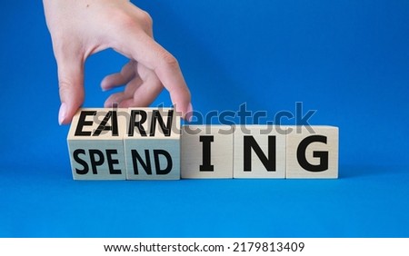 Earning and Spending symbol. Businessman hand. Turned cubes with words Earning and Spending. Beautiful blue background. Business and Earning and Spending concept. Copy space
