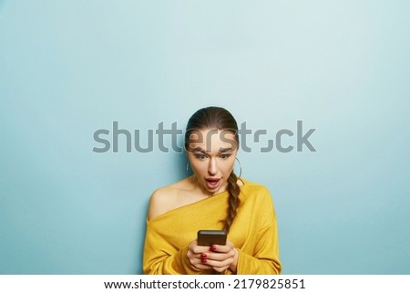 Happy surprised woman uses mobile phone,  isolated over blue background. Mobile communication