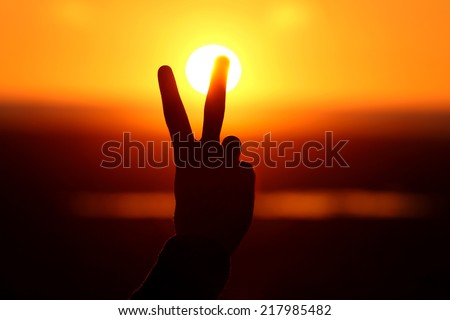 Silhouette of hand with two fingers at sunset 