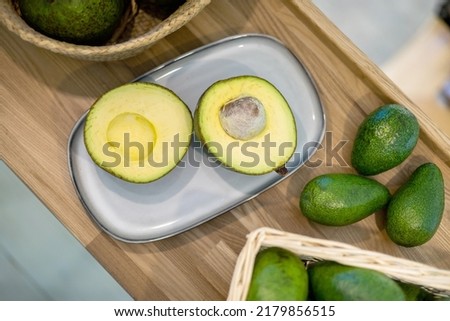 Organic farm avocado in straw basket on wooden table closeup. Fresh ripe green exotic fruits full of healthy nutriment vegetarian eating. Three tropical edible plant with twig for guacamole cooking Royalty-Free Stock Photo #2179856515