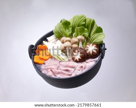 Shabu-shabu or Sukiyaki in hot pot with sliced meat and fresh vegetables on a light gray background Royalty-Free Stock Photo #2179857661