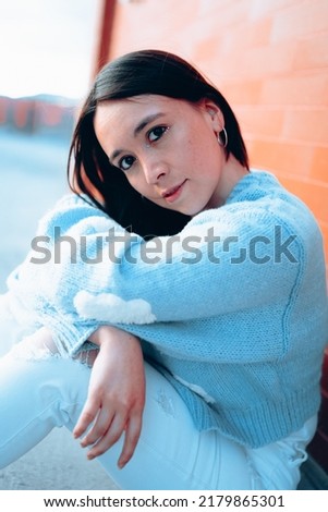 latin woman with black hair, sitting with arms crossed smiling while looking at the camera, natural beauty of the face, studio