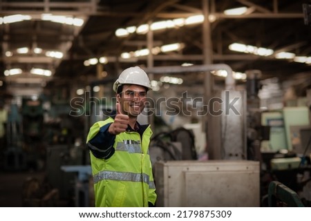 Happy Young Indian male engineer wearing safety workwear standing in the factory and thumbs up to appreciate the success of the teamwork. safety first in the industrial plant.
