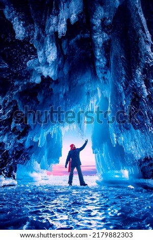 Adventure travel winter Lake Baikal tourist man with red scarf background ice grotto and cave, frozen icicles.