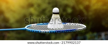 White cream badminton shuttlecock and blue badminton racket with outdoor blurred trees and public park background, concept for outdoor recreational sport activities.