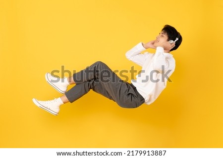 Young good looking asian man floating while listen with headphone isolated on yellow background Royalty-Free Stock Photo #2179913887