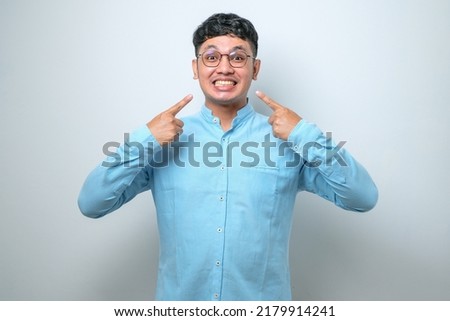 Young handsome asian man wearing casual shirt standing over isolated white background smiling cheerful showing and pointing with fingers teeth and mouth. Dental health concept.