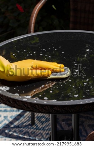 Person wearing rubber gloves cleaning a glass top patio table in a garden backyard