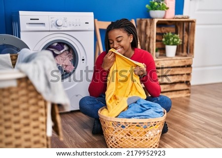 African american woman smelling towel washing clothes at laundry room Royalty-Free Stock Photo #2179952923