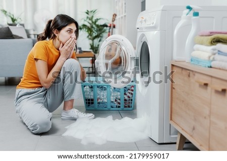 Woman checking her damaged washing machine, the floor is flooded Royalty-Free Stock Photo #2179959017