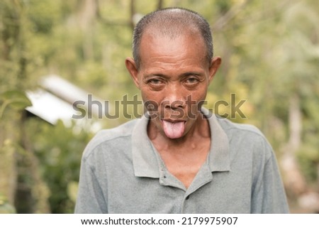 A balding Filipino man teasing and mocking someone. A simpleton sticking his tongue out. Outdoor scene. Royalty-Free Stock Photo #2179975907