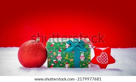 
Christmas package with a bauble and a poinsettia in the snow against a red background