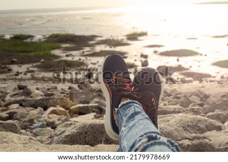 girl sits by the lake, wears on her feet sneakers. Female legs take rest and relax