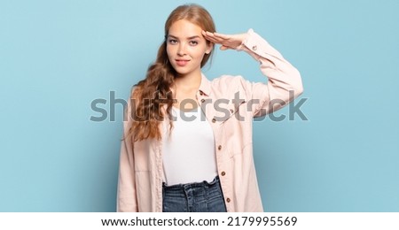 blonde pretty woman greeting the camera with a military salute in an act of honor and patriotism, showing respect Royalty-Free Stock Photo #2179995569
