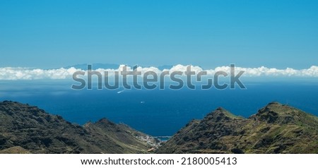 Long narrow band of cloud as a line between sky and ocean. Panoramic picture. Rocky landscape at the foreground.