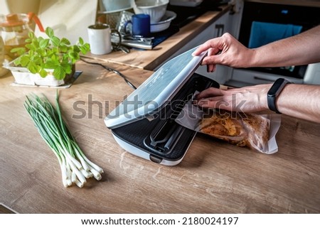 Woman using vacuum seal machine for vacuum packing meat in plastic bags. Bunch of green onion on the table Royalty-Free Stock Photo #2180024197
