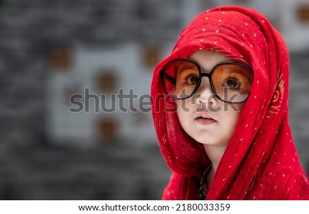 Cute Indian baby girl wrapped in red scaref  andwearing yellow transparent goggles looking in front of the camera