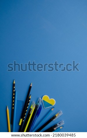 Flatlay left vertical composition black pencils, yellow pencil, blue ruler, patch heart and blank blue background