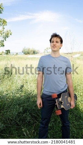 cool young man with grey shirt posing with longboard, skateboard outdoors, in park and is happy