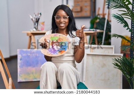African young woman holding painter palette smiling happy and positive, thumb up doing excellent and approval sign 