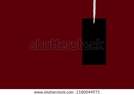 A blank black label or price tag against a red background. Space for text. Close-up photo. Shopping and price tag concept
