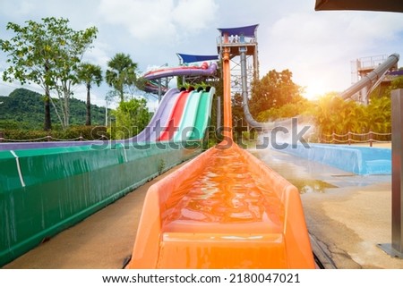 Colorful plastic pipe attraction sliders (focus at orange slider) in the water park with people in a water playground, sunlight background . Vacation concept