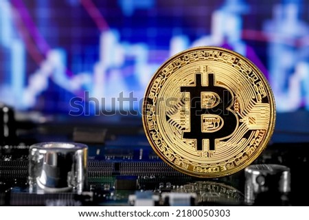 Close-up of a metallic golden Bitcoin cryptocurrency coin standing on a computer board against the background of a colorful computer stock chart