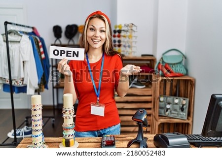 Young caucasian woman holding banner with open text at retail shop celebrating achievement with happy smile and winner expression with raised hand 